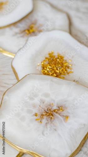 Cup holder, epoxy resin tray, stone cut, white marble with gold trim. White streaks of paint. Table setting decor, object aesthetics. Gloss, reflection. Stone effect. Blurred background. 