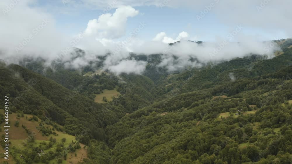 Aerial view, on green forest and fog in mountains. Slow flight over trees, hills against backdrop white clouds and blue sky, natural light. Beautiful landscape pristine nature. Europe drone flight Aerial view, on green forest and fog in mountains. Slow flight over trees, hills against backdrop white clouds and blue sky, natural light. Beautiful landscape pristine nature. Europe drone flight