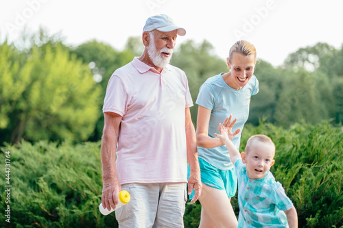 Summer, sport, outdoor activities concept. Happy and cheerful grandfather walking outdoor with his daughter and grandson. Portrait of multi generation family spending time together in park. © Iryna