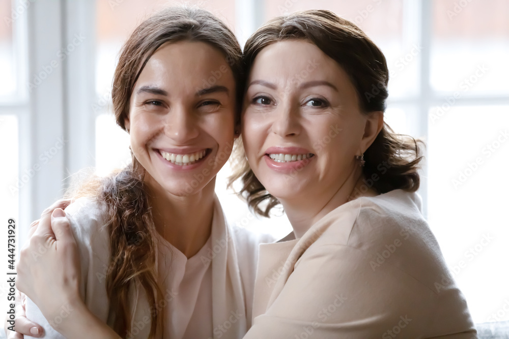 Close up headshot portrait of smiling middle-aged Caucasian mother and grownup daughter hug cuddle relax at home together. Profile picture of happy older mom and adult girl show family love and care. Close up headshot portrait of smiling middle-aged Caucasian mother and grownup daughter hug cuddle relax at home together. Profile picture of happy older mom and adult girl show family love and care.