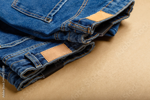 Classic blue jeans. Casual pants clothing blue jeans with brown blank leather labels on beige craft background with copy space