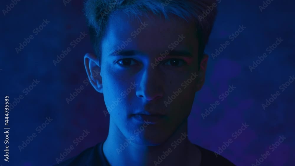Portrait of a handsome young man on a black background in neon light and red light flashing on his face. 4K video Portrait of a handsome young man on a black background in neon light and red light flashing on his face. 4K video