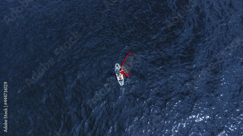 A man on an inflatable board with a sail in the middle of the water. Windsurfing. Top View