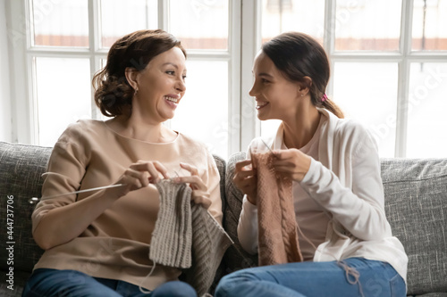 Smiling old Caucasian mother and adult daughter sit relax on couch at home have fun rest knit with needles together. Happy middle-aged mom and grownup girl child enjoy family weekend hobby activity. photo