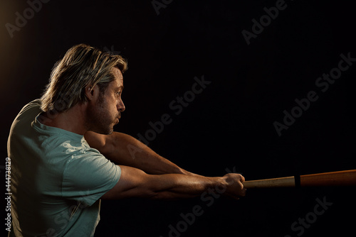 Blonde man with a stubble beard in a light green t-shirt hits with a baseball bat. Side view.