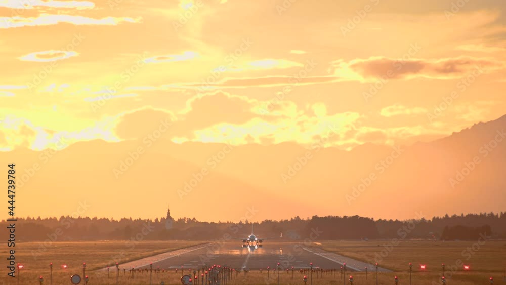 Large passenger airplane takes off. View of long runway, Ljubljana airport, Slovenia. Dramatic and colorful sunset. Aircraft taking off facing towards the camera. Static, real time Large passenger airplane takes off. View of long runway, Ljubljana airport, Slovenia. Dramatic and colorful sunset. Aircraft taking off facing towards the camera. Static, real time
