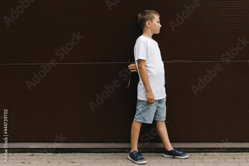 Young teenager dressed in white t-shirt and posing outdoor near brown wall . Mock up. Space for logo, text, image. Lifestyle, summer time.  © MarijaBazarova