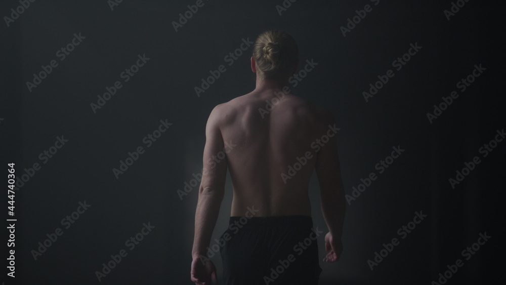 Fototapeta premium Male athlete walking in dark corridor. Sporty guy going in loft building