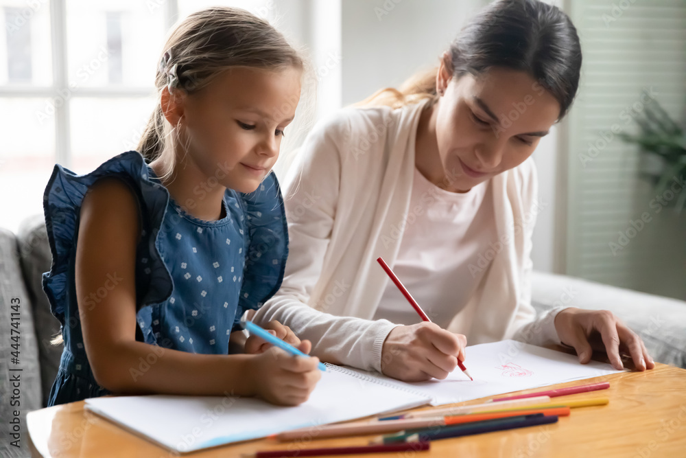 Caring young Caucasian mother and little teen daughter sit at table at home draw paint in album with pencils. Loving happy mom have fun enjoy learning hobby activity with small girl child together. Caring young Caucasian mother and little teen daughter sit at table at home draw paint in album with pencils. Loving happy mom have fun enjoy learning hobby activity with small girl child together.