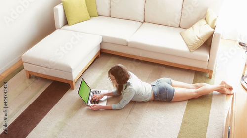 Relaxing at home. Beautiful young woman using her laptop while lying on carpet at home. Green screen.