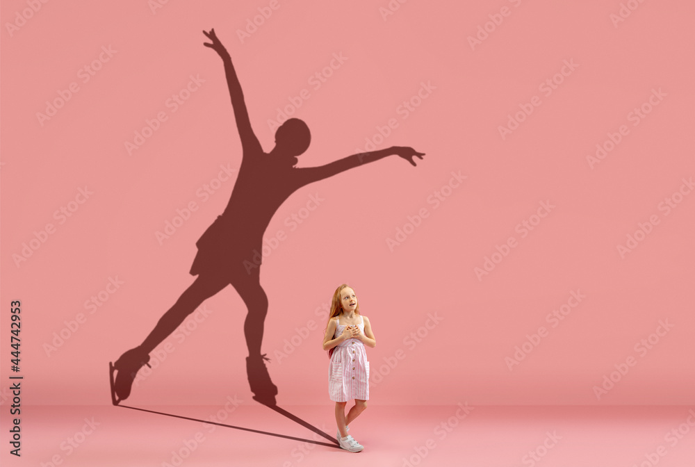 Childhood and dream about big and famous future. Conceptual image with girl and shadow of female figure skater on coral pink wall, background.