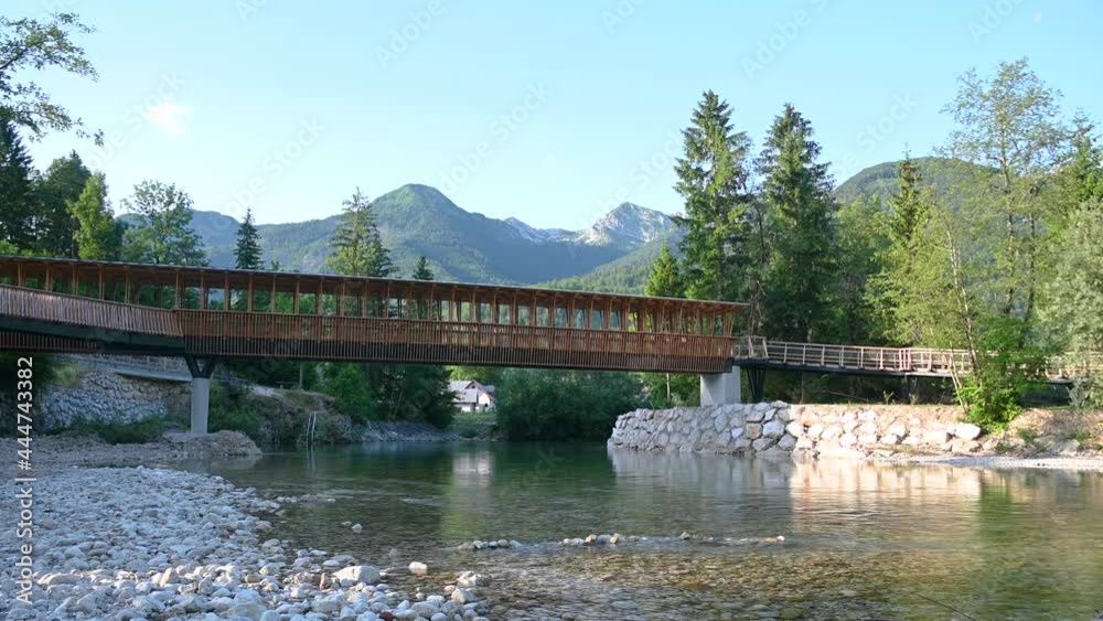 Low angle view of new wooden walkway bridge in Slovenia. Beautiful river flowing in pristine nature. Summer in Alpine valley. Static shot, wide angle Low angle view of new wooden walkway bridge in Slovenia. Beautiful river flowing in pristine nature. Summer in Alpine valley. Static shot, wide angle