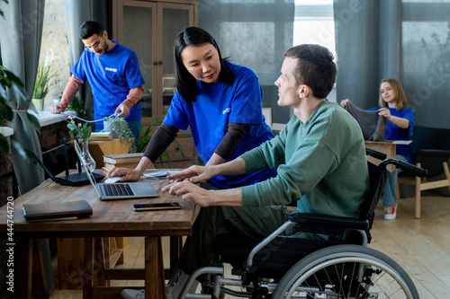 Asian woman in volunteer t-shirt helping young disabled man with connection