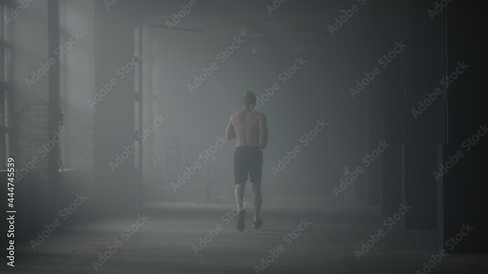 Muscular man doing cardio workout in loft building. Guy running in corridor