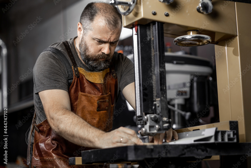 Brutal master carpenter saws wooden blanks on machine in workshop