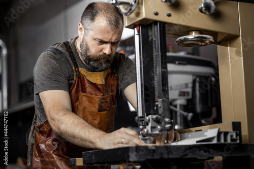 Brutal master carpenter saws wooden blanks on machine in workshop