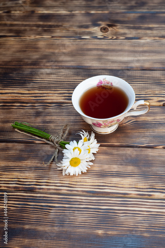 Cup of chamomile tea and chamomile flowers on wooden background. Close-up.