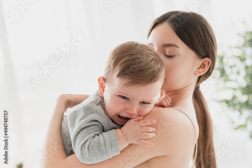 Young single mother lulling cradling her crying little small son daughter toddler infant newborn baby. Colics, teething health problems. Postnatal depression. Motherhood and childcare photo