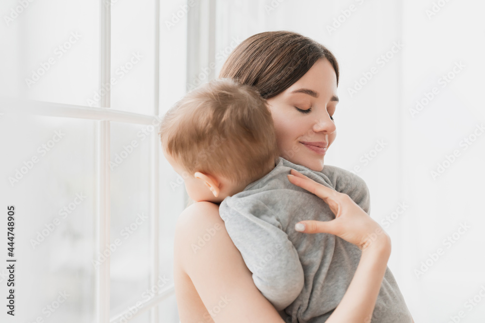 Young single mother lulling cradling her little small son daughter toddler infant newborn baby putting to sleep her kid child, napping and bedtime. Motherhood and childcare concept Young single mother lulling cradling her little small son daughter toddler infant newborn baby putting to sleep her kid child, napping and bedtime. Motherhood and childcare concept