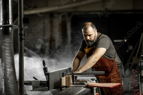 Brutal master carpenter saws wood blanks on machine in workshop