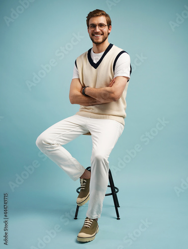 Feeling comfortable. Joyful positive young man sitting on a stool and smiling isolated on blue. photo