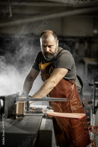 Brutal master carpenter saws wood blanks on machine in workshop