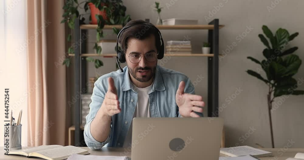 Smart young man in eyeglasses wearing wireless headphones with microphone, holding video call conversation using web camera zoom software application on computer, discussing working issues distantly.