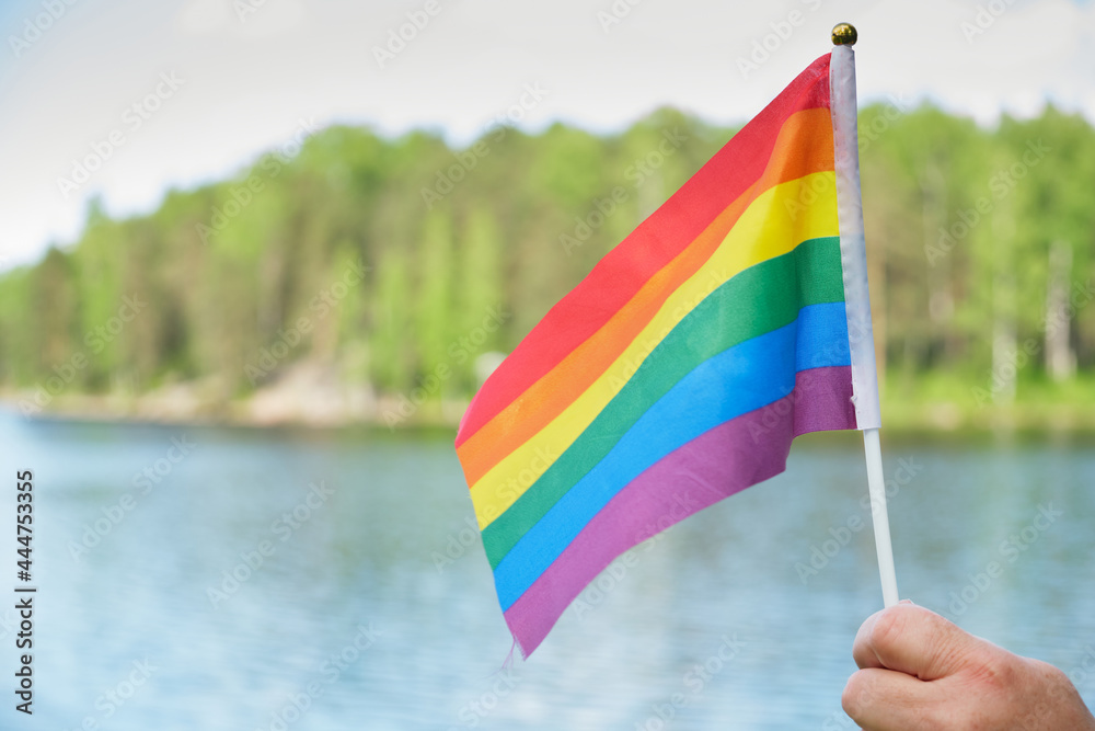flag symbol of the lgbt community on a background of grass and trees, flag in woman's hand flag symbol of the lgbt community on a background of grass and trees, flag in woman's hand