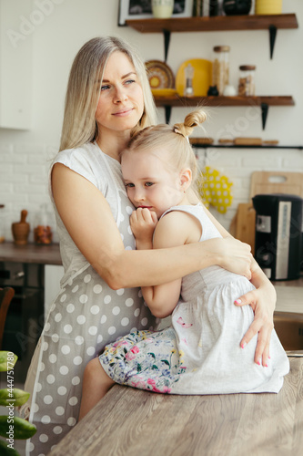 Young beautiful woman hugs and kisses her cute little daughter