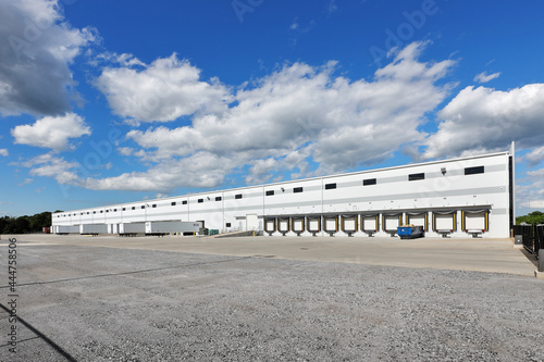 Rear view of large white distribution warehouse industrial building with parking lot