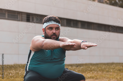 a fat man doing a squat outdoors.