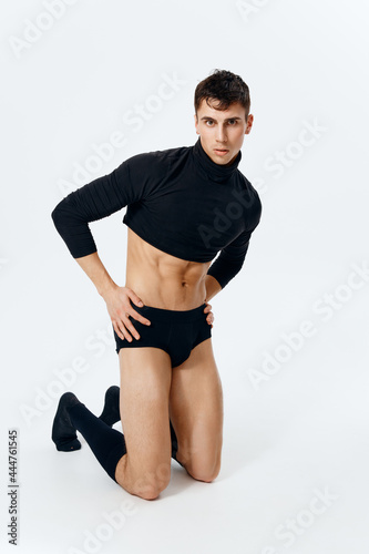 a man with an athletic physique in a sweater underpants and socks stands on a light background
