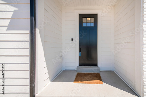 Exterior of a house with a view of black wooden door with glass panel and an enginered wood sidings