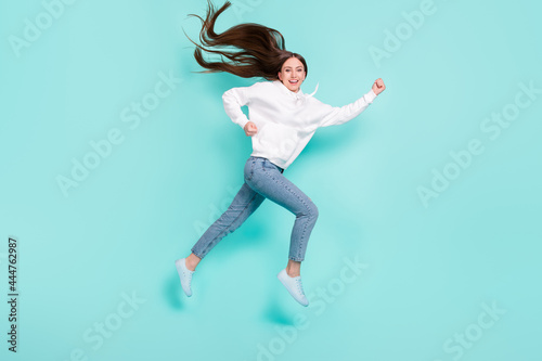 Full length body size view of pretty cheerful motivated girl jumping running isolated over bright teal turquoise color background © deagreez