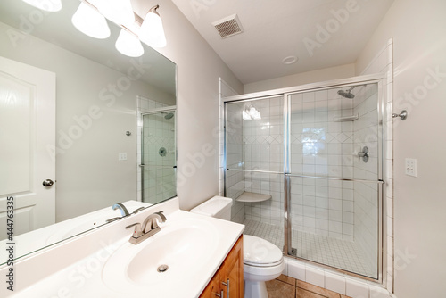 Interior of a bathroom with wooden vanity sink with tile counter and shower stall with glass