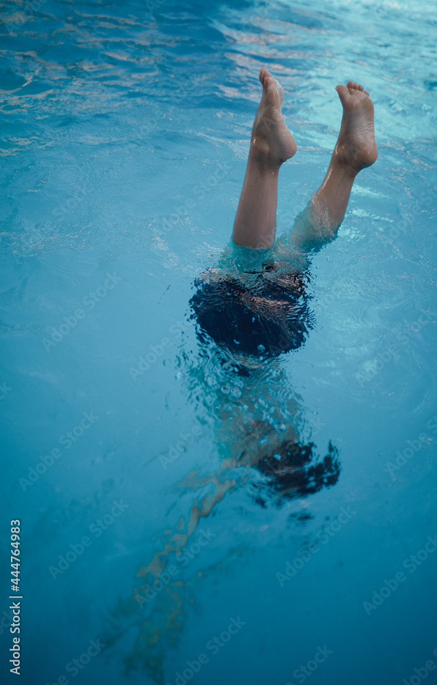 A child dips his head into the water, feet look out of the water.