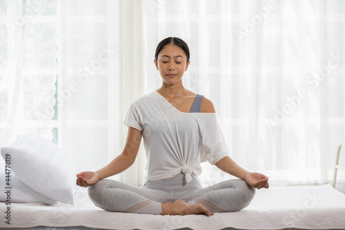 Calm of wellness Asian young woman sit on bed breathing with yoga lotus pose,Yoga meditation of young healthy woman relax and comfortable at white cozy home,Yoga Exercise for Wellness Concept © 220 Selfmade studio