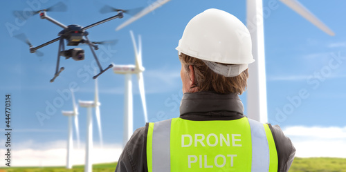 professional licenced drone operator engineer with hardhat and safety vest piloting at wind power turbine generator park
