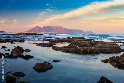 scenic view of table mountain in capetown south africa from bloubergstrand at sunset with sea and rocks in foreground