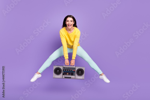 Full length body size view of pretty cheerful girl jumping holding boom box having fun isolated over violet purple color background