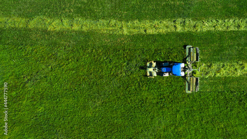 Aerial view of a tractor mowing a green field with fresh grass. Tractor cleaning of excess grass from the field.