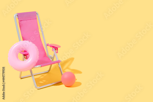 Fototapeta a pink beach chair with a pink float and a ball on yellow background