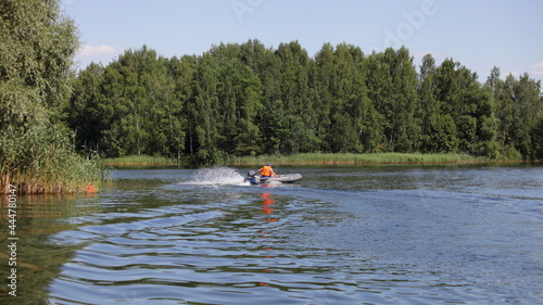 Inflatable motor boat with outboard motor fast floating on the water on green trees background at Sunny summer day, beautiful West Russian river landscape
