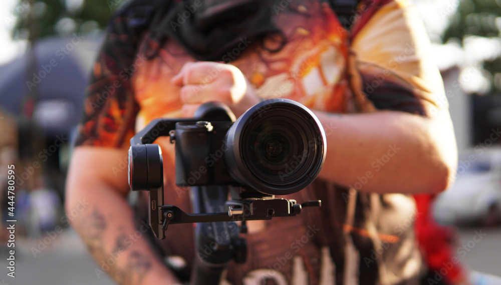 A man with a camera and a lens. Photocamera on the stabilizer for video shooting. Blurred background and sun glare A man with a camera and a lens. Photocamera on the stabilizer for video shooting. Blurred background and sun glare