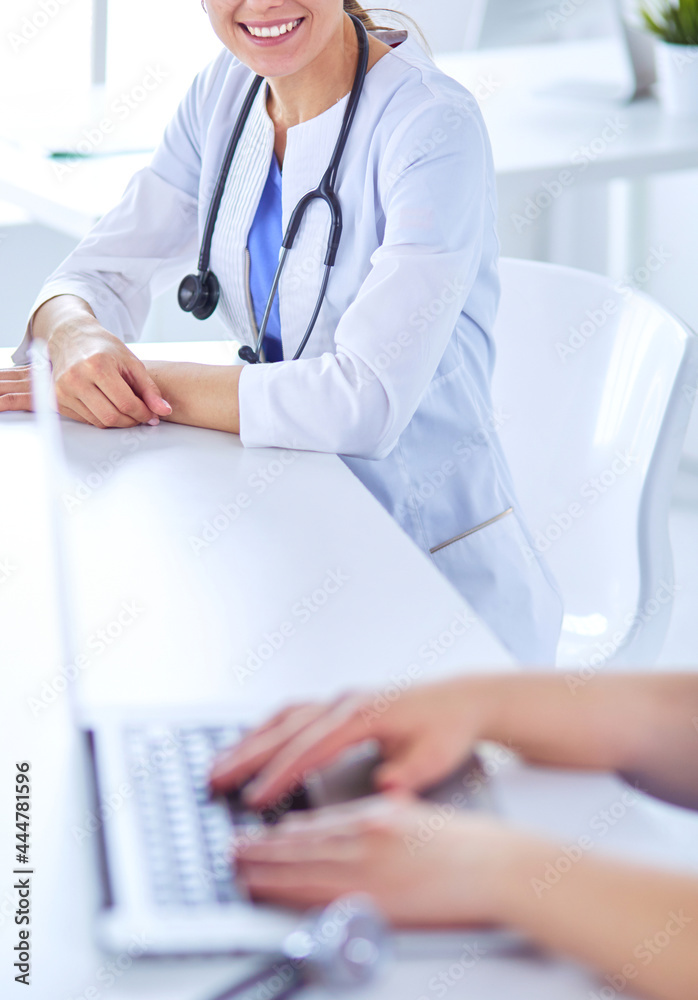 Smiling doctor using a laptop working with her colleagues in a bright hospital room Smiling doctor using a laptop working with her colleagues in a bright hospital room