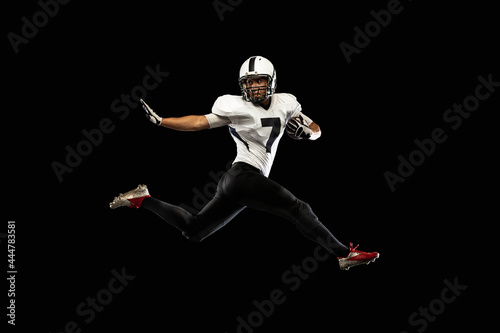 Portrait young American football player, athlete in black white sports uniform training isolated on dark studio background. Concept of professional sport, championship, competition. © master1305