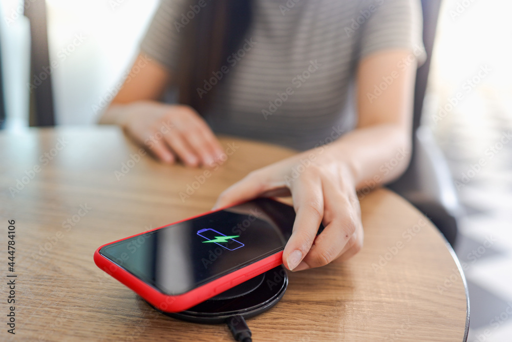 Fototapeta premium Charging mobile phone battery with wireless device in the table. Smartphone charging on a charging pad. Mobile phone near wireless charger.