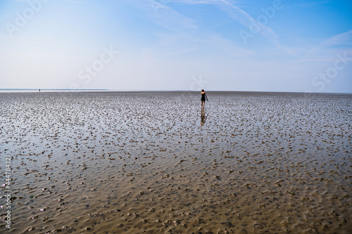 wide shot of lonesome girl walking through the beautiful wadden sea with sun shining and blue sky at sahlenburg, cuxhaven photo