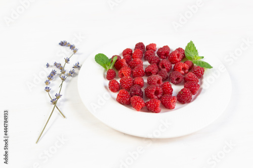 Ripe red raspberries on white plate with mint leaves and lavender