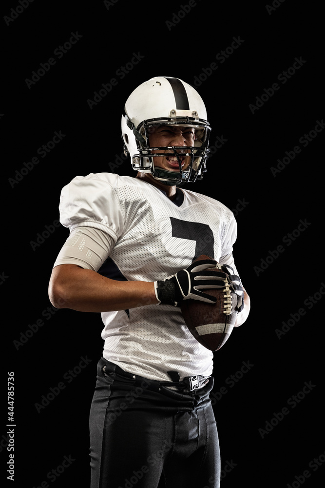 Portrait young American football player, athlete in black white sports uniform posing isolated on dark studio background. Concept of professional sport, championship, competition.